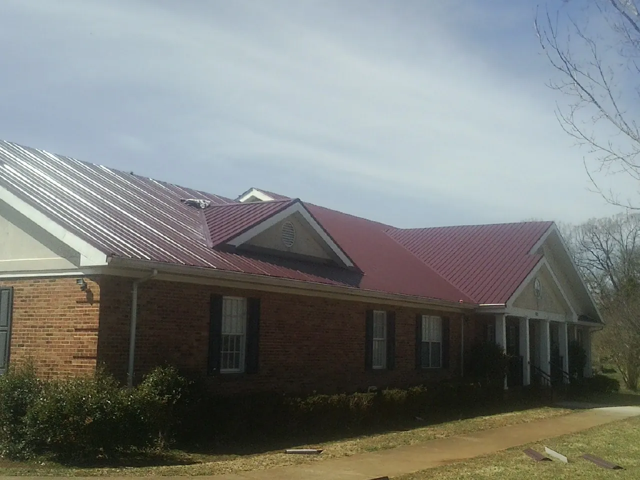 Red metal roof with gabled entries on a long brick building, from a Hail Damage Roof Repair job in Albany